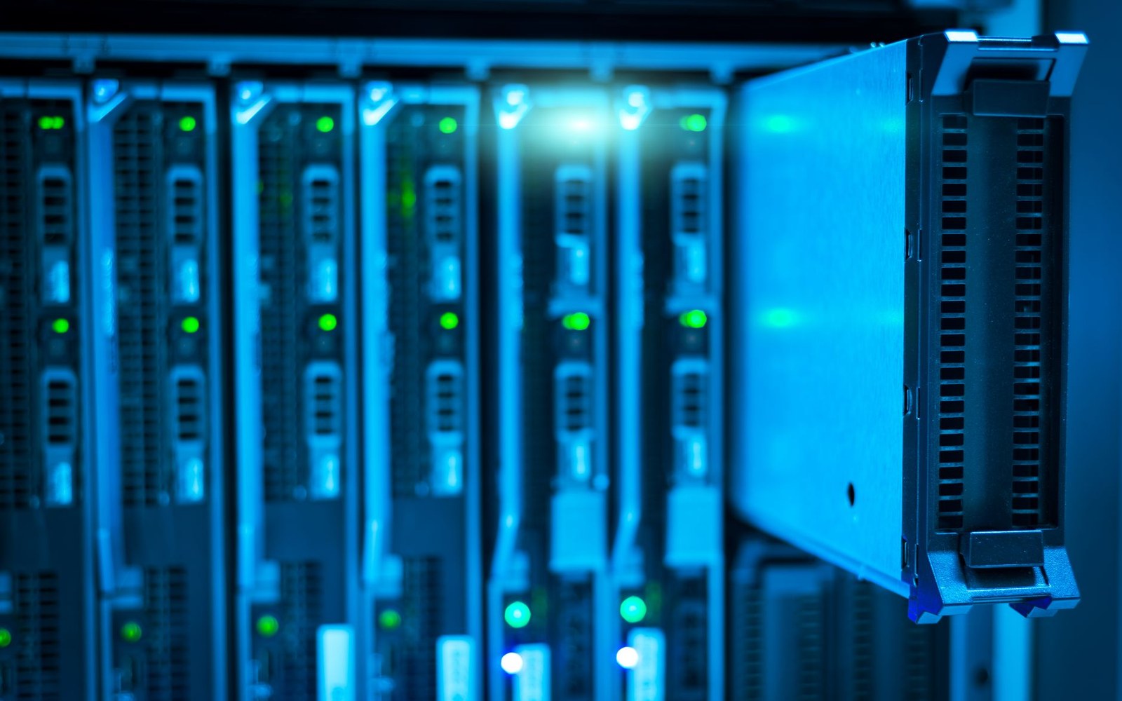 A data-centre aisle with server rack indicator lights, an adult technician in the middle distance walking between racks